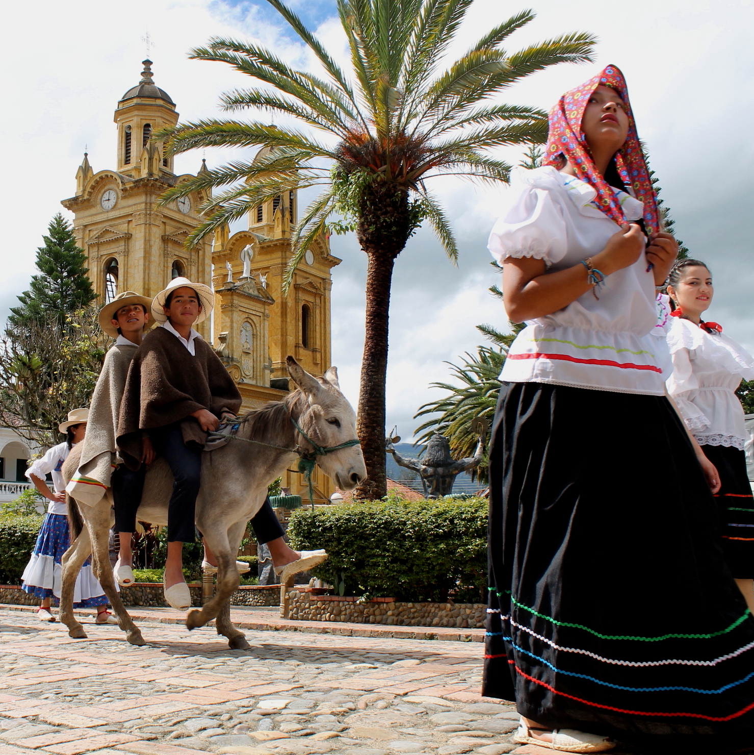 Mujer con traje típico boyacense y arrieros con burro en el parque principal de Jenesano
