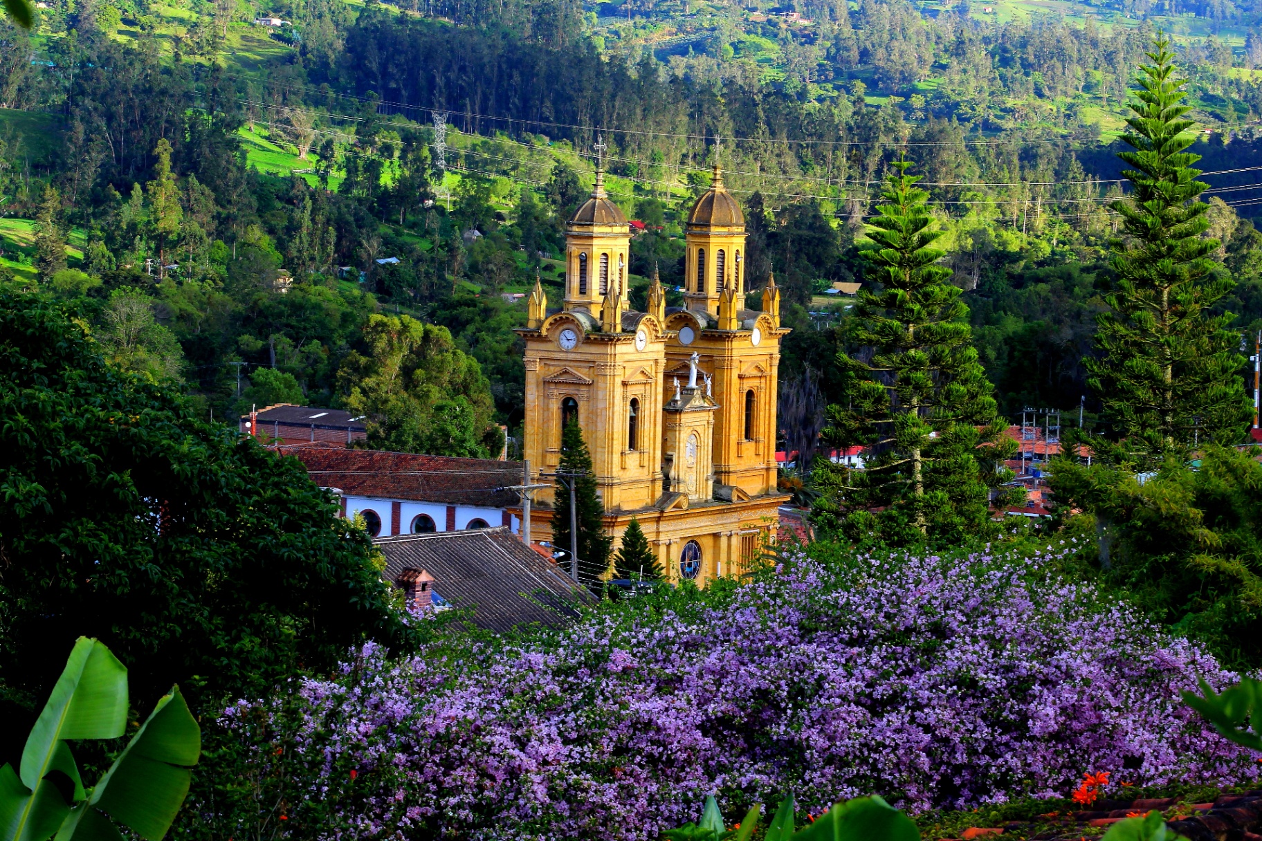 Iglesia colonial amarilla de Jenesano entre montañas verdes y flores moradas, Boyacá