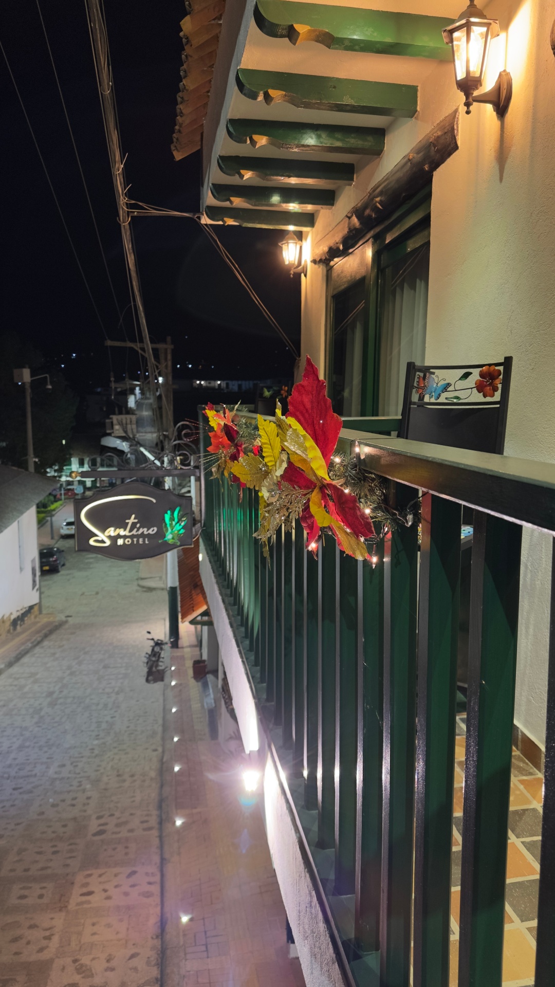 Balcón del Hotel Santino con letrero iluminado en la noche y detalles verdes