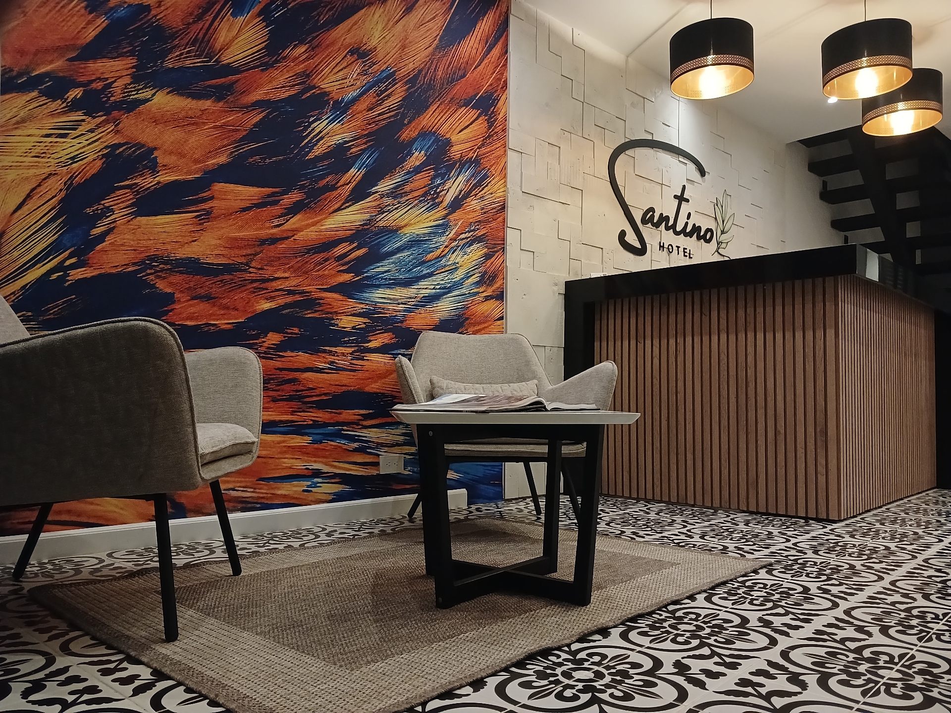 Recepción de Hotel Santino con mural artístico de colores vibrantes, sillón de espera y logo Santino — Jenesano, Boyacá